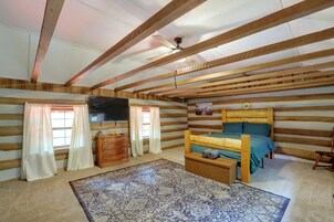 A log cabin room with a bunk bed, wooden beams, a ceiling fan, a dresser, and a patterned rug.