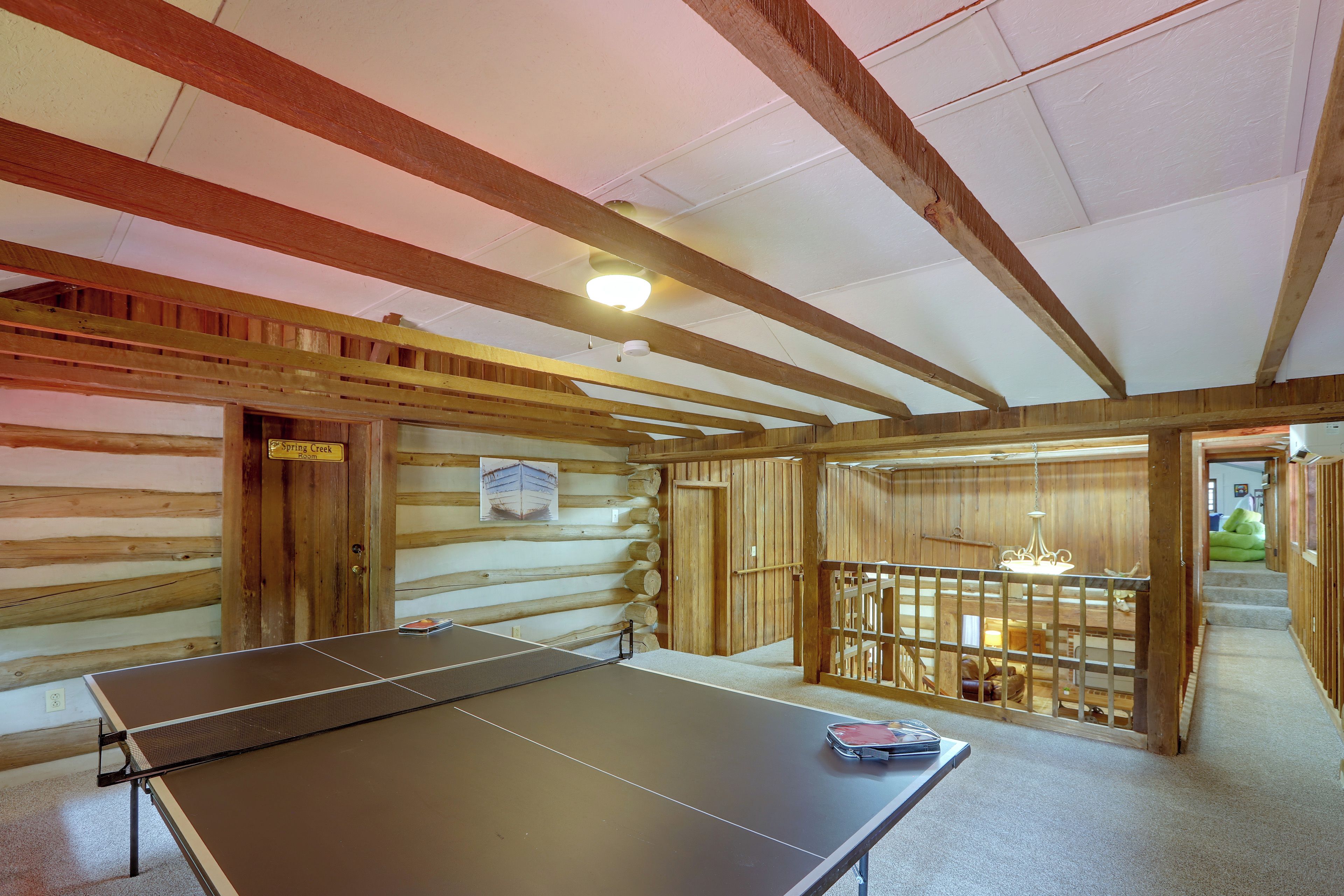 A room with a ping pong table, wooden walls, and a ceiling with exposed beams.