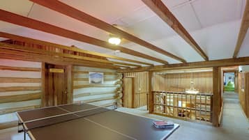 A room with a ping pong table, wooden walls, and a ceiling with exposed beams.