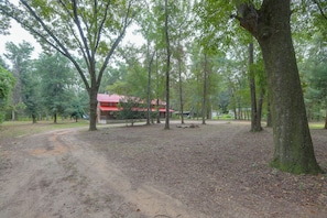 A forested area with a dirt path leading to a building with a red roof. - Across From Marina! Over 4k Sq Ft Lodge! (Bainbridge)