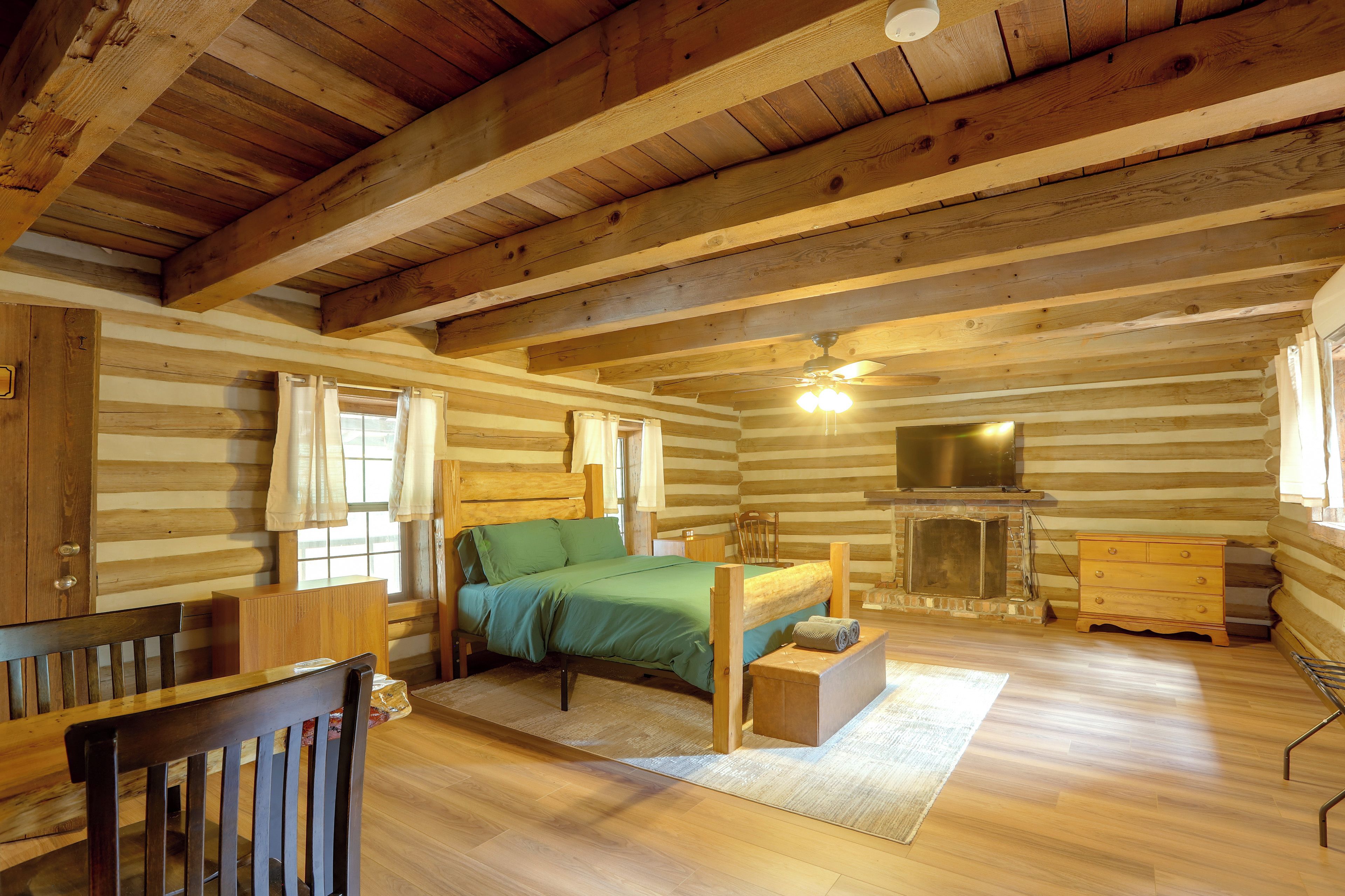 A log cabin bedroom with a bed, dresser, and a fireplace.