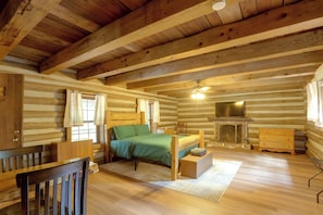 A log cabin bedroom with a bed, dresser, and a fireplace.