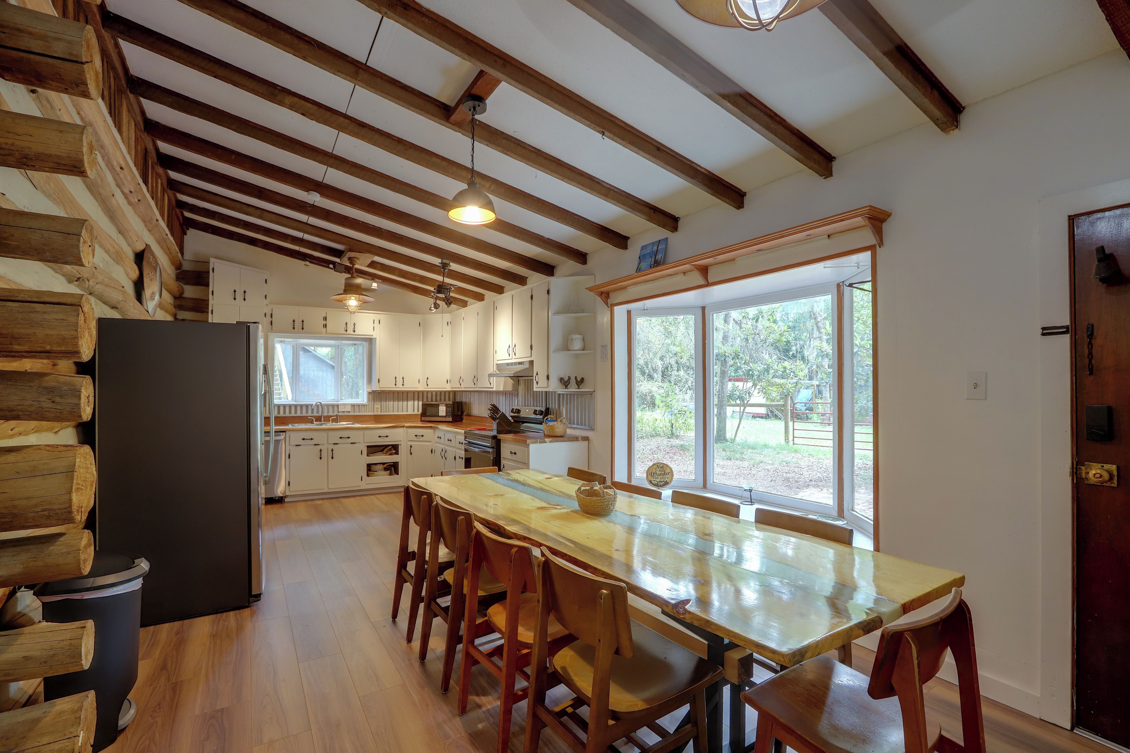 A kitchen with wooden beams, a dining table with chairs, and a view through the window.
