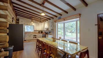 A kitchen with wooden beams, a dining table with chairs, and a view through the window.