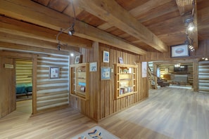 A log cabin interior with wooden walls, a central wooden display case, and a staircase leading to another level. - Across From Marina! Lake Seminole Fishing Lodge (Bainbridge)