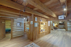 A log cabin interior with wooden walls, a central wooden display case, and a staircase leading to another level.
