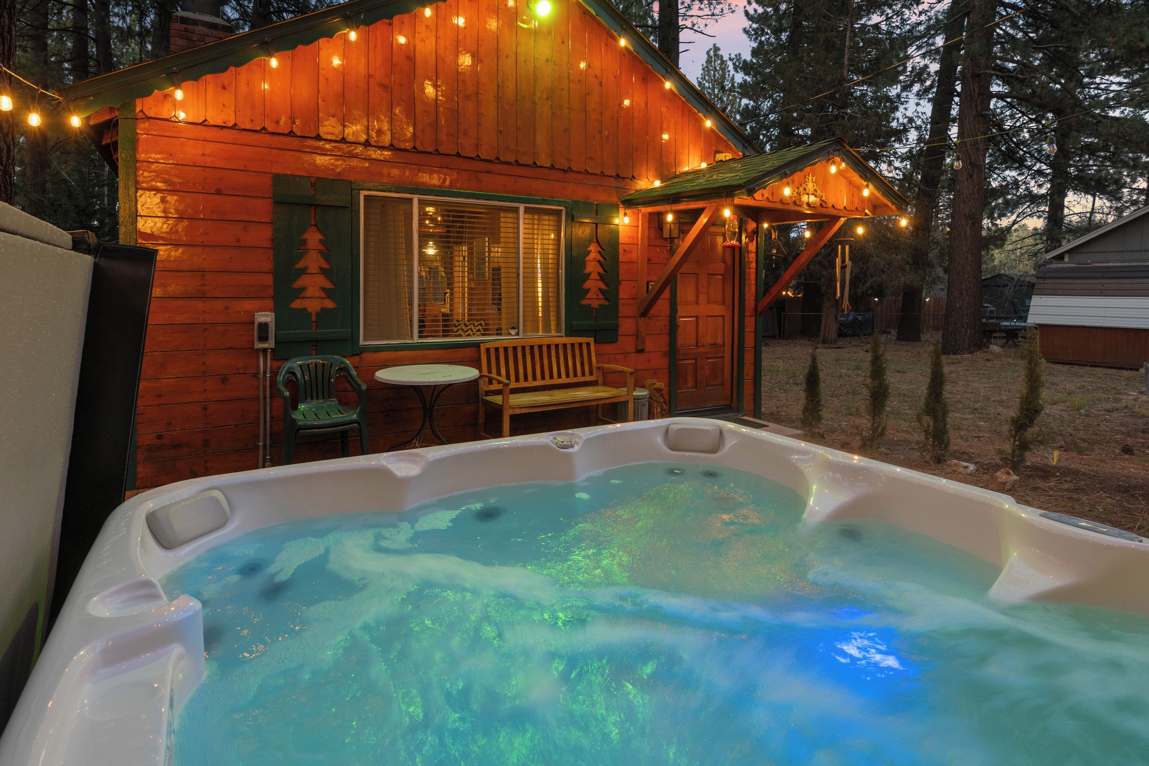 Una cabaña de madera con jacuzzi, terraza y luces colgantes.