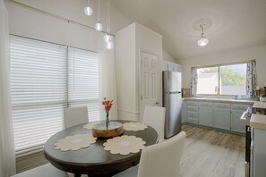A kitchen with a dining table, chairs, a refrigerator, and a window with curtains. - The Iola / Chic Vintage Glam & Modern Comfort (Lubbock)