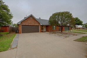 A residential house with a brick facade, a garage, and a front yard with a tree and a stone pathway. - The Iola / Chic Vintage Glam & Modern Comfort (Lubbock)
