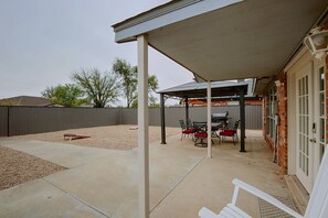 A covered patio area with a barbecue grill, outdoor seating, and a view of the backyard. - The Iola / Chic Vintage Glam & Modern Comfort (Lubbock)