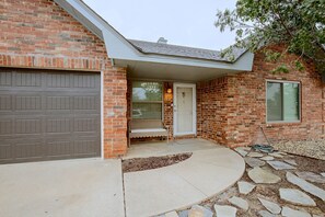 A residential building with a brick facade, a garage door, a front porch with a bench, and a stone pathway leading to the entrance.