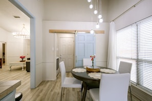 A dining area with a round table, white chairs, a chandelier, and a door with a wooden frame. - The Iola / Chic Vintage Glam & Modern Comfort (Lubbock)