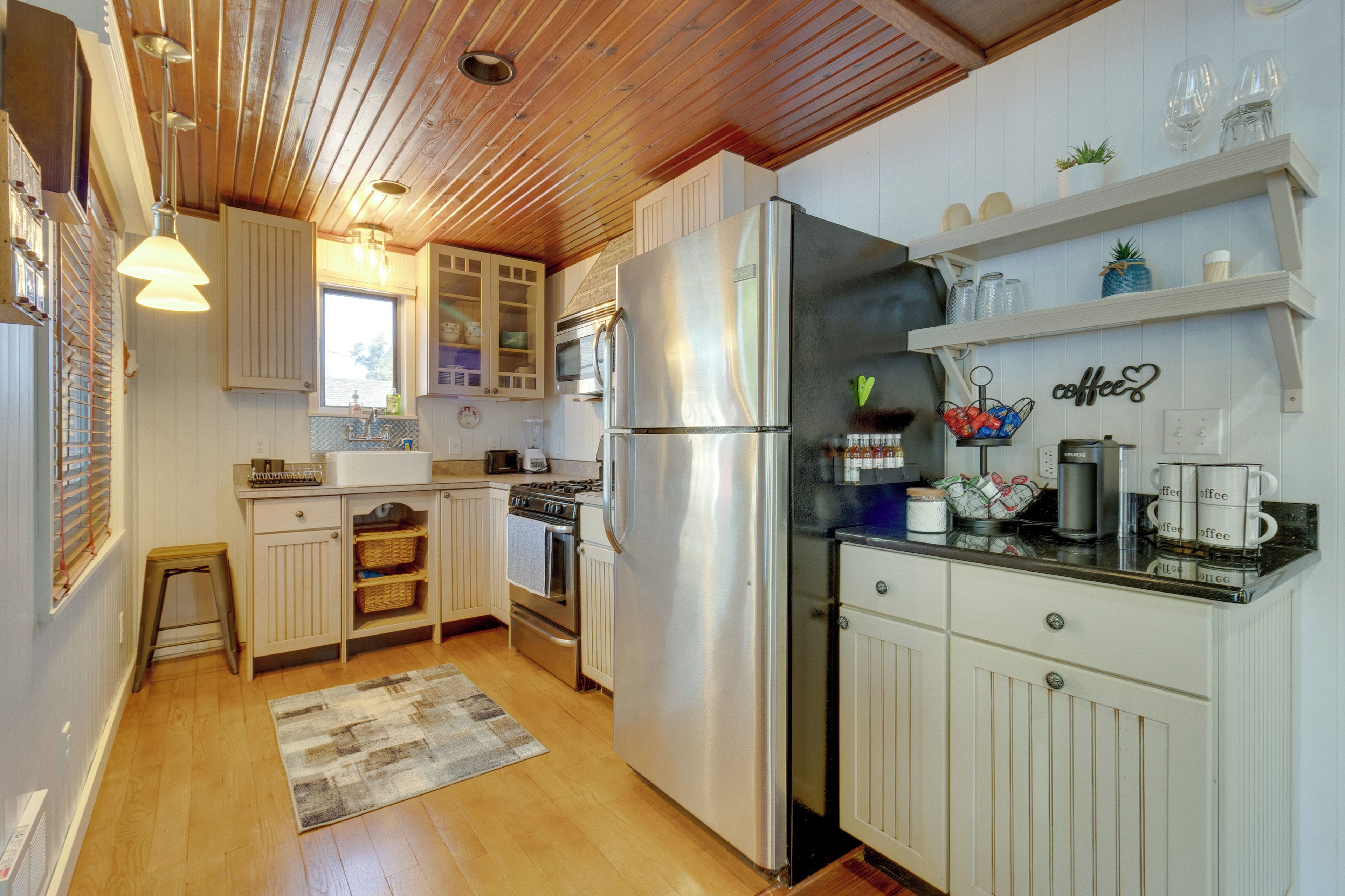 A compact kitchen with wooden cabinets, a stainless steel refrigerator, and a coffee station.