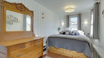 A bedroom with a wooden dresser, a bed with a quilted cover, a mirror with decorative carvings, and a ceiling light fixture.