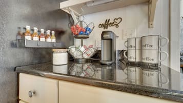 Una encimera de cocina con una estación de café, que incluye una cafetera Keurig, tazas de café y una cesta con sobres de café.