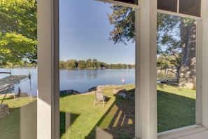 A view through a screened door of a lakeside property with a deck, chairs, and a flamingo statue. - Fun in the Sun/firepit Fires/sunsets/relaxing (Pleasant Lake)