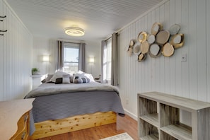 Une chambre à coucher avec un lit en bois, une table de chevet, un luminaire fixé au mur et une fenêtre avec des rideaux.