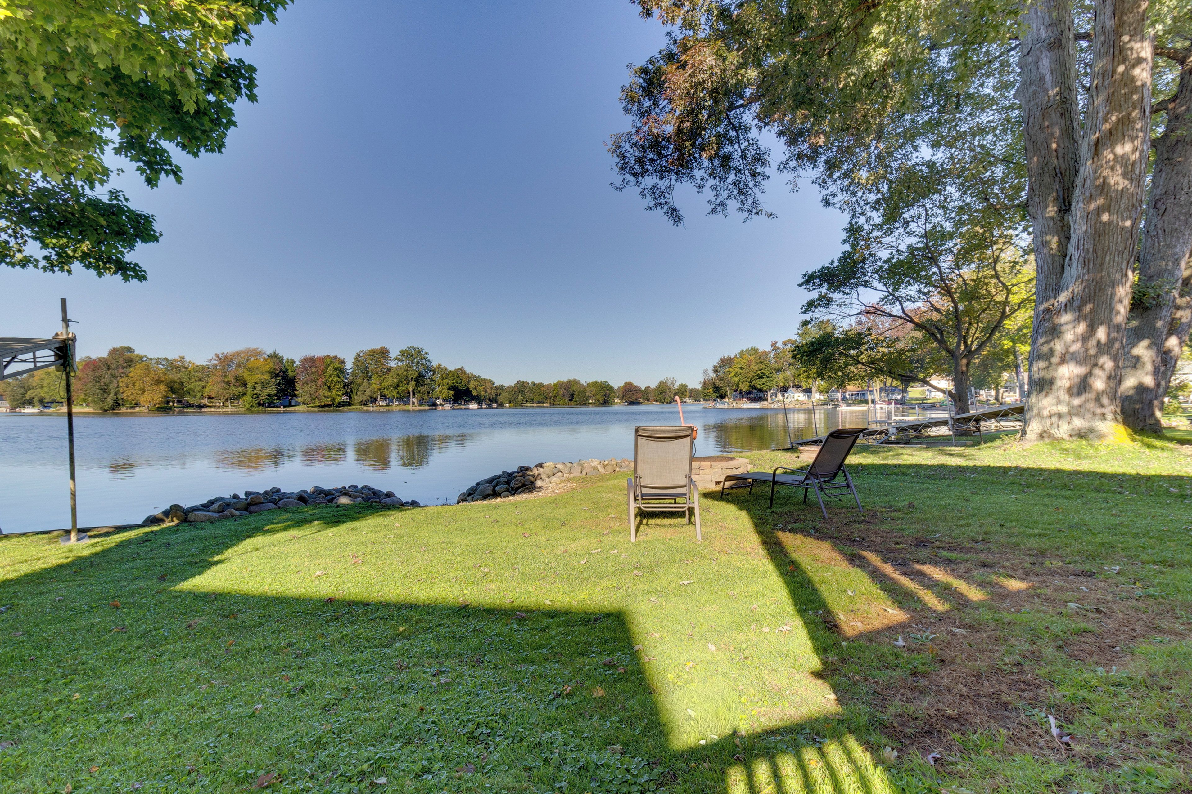 A lakeside view with a grassy area, a chair, and a bench.