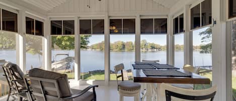 A covered outdoor seating area with a view of a lake, furnished with chairs and a table.