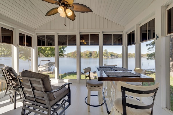 A covered outdoor seating area with a view of a lake, furnished with chairs and a table. - Fun in the Sun/firepit Fires/sunsets/relaxing (Pleasant Lake)