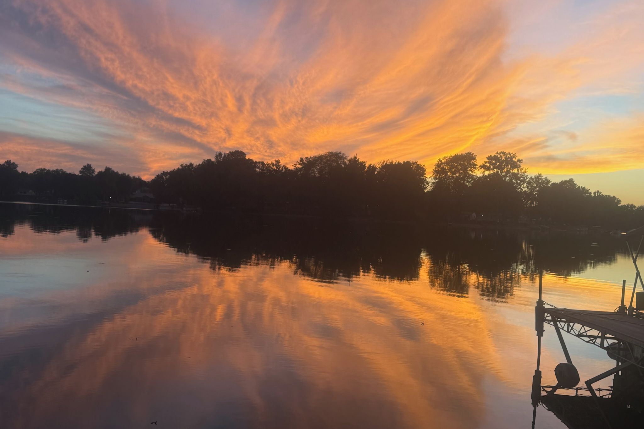 A calm lake at sunset with a dock on the right.