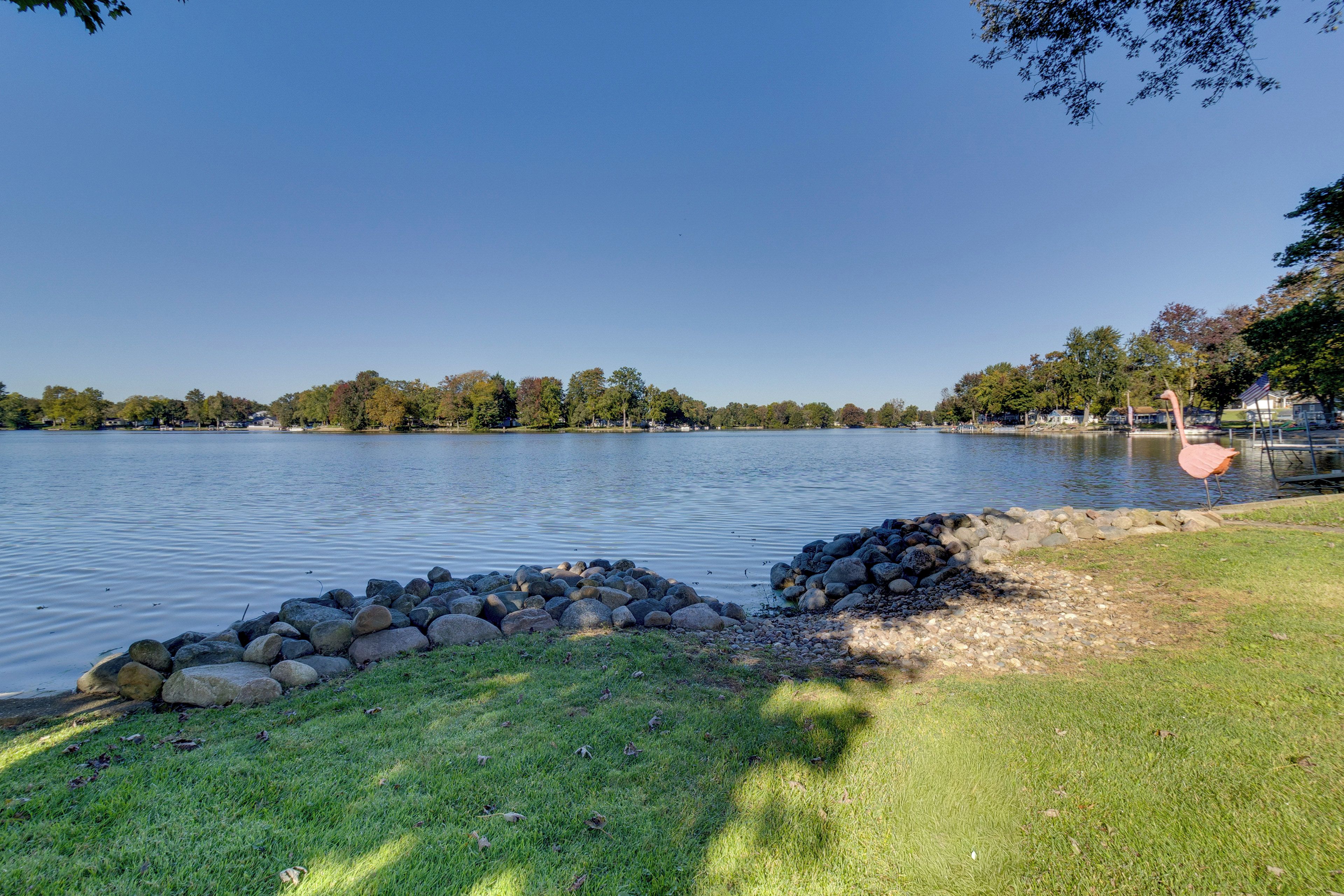 A lake with a grassy shore, a stone wall, and trees in the background.