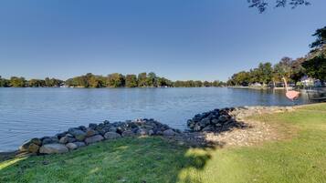 A lake with a grassy shore, a stone wall, and trees in the background.