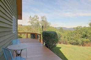 Una terraza de madera con una mesa y sillas, con vista a un patio cubierto de césped y árboles.