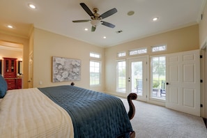 A bedroom with a bed, a ceiling fan, a painting, and a view through the door.