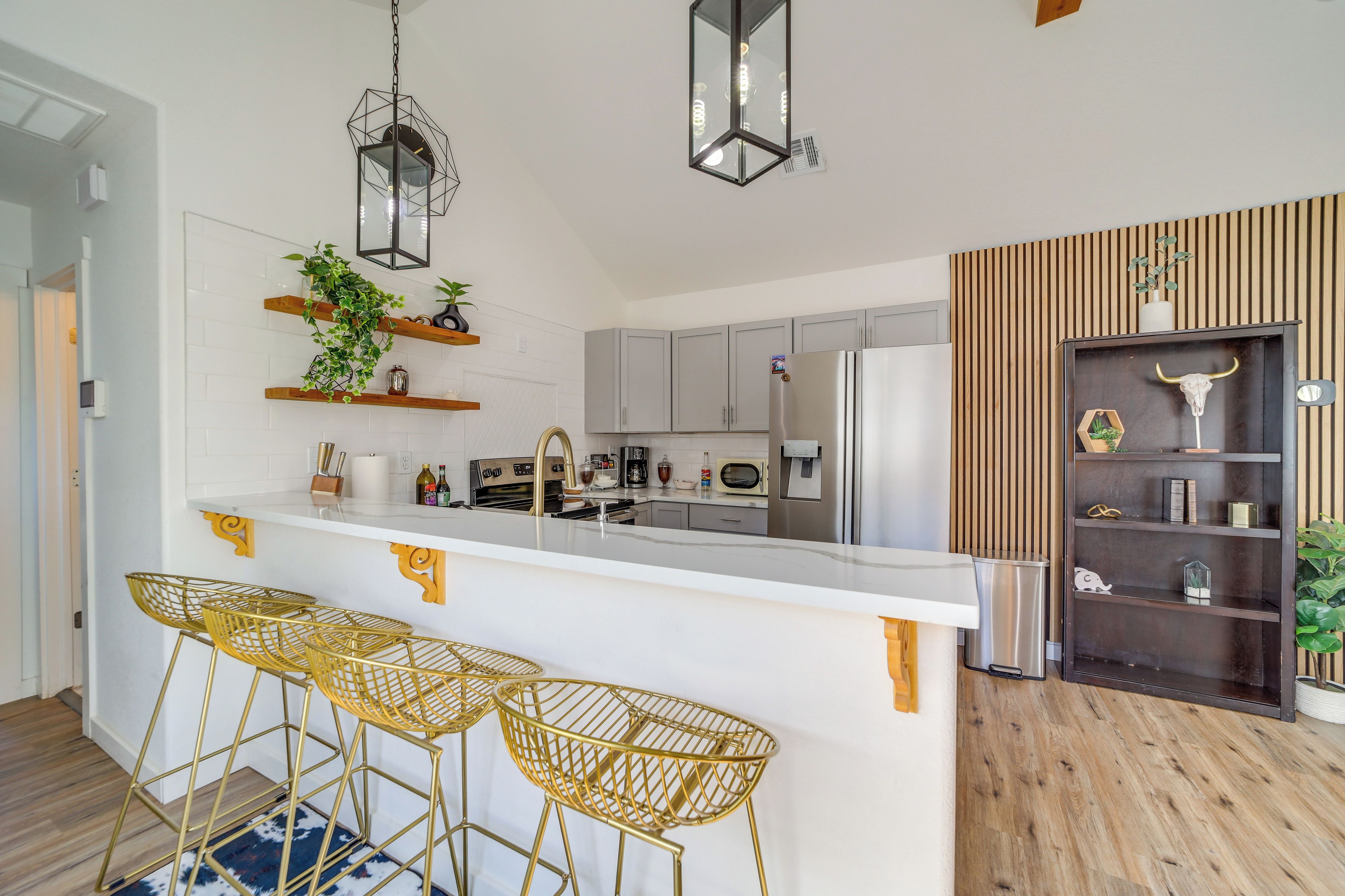 A modern kitchen with a central island, bar stools, and a decorative shelf with plants.