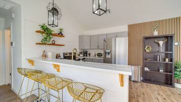 A modern kitchen with a central island, bar stools, and a decorative shelf with plants.