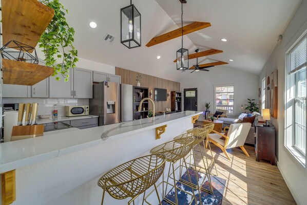A modern kitchen with a central island, bar stools, and a dining area with a sofa and chairs.