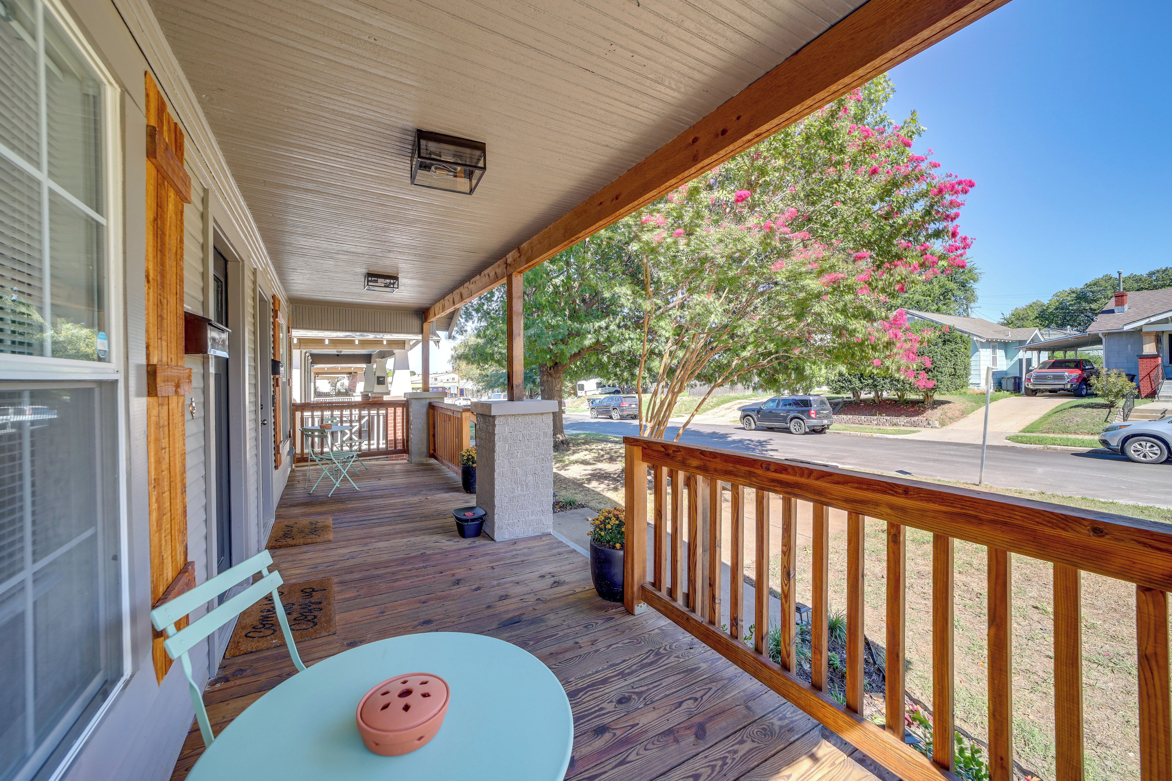 A covered porch with a wooden railing, a table with a chair, and a potted plant.