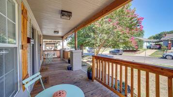 A covered porch with a wooden railing, a table with a chair, and a potted plant.