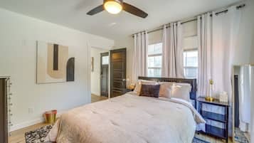 A bedroom with a bed, a nightstand, a mirror, a ceiling fan, and a window with curtains.