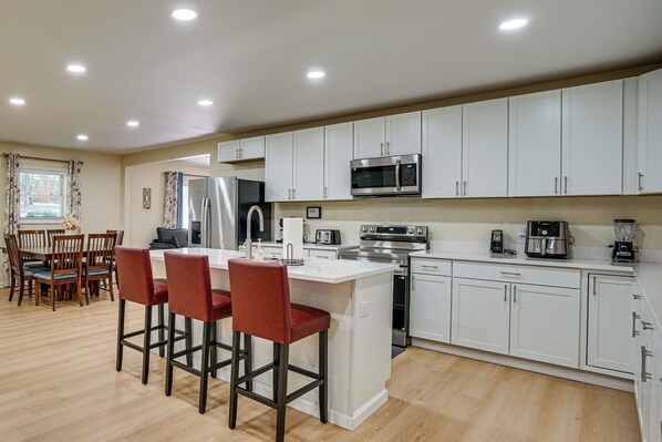 A modern kitchen with white cabinets, stainless steel appliances, and a wooden dining area with red chairs.