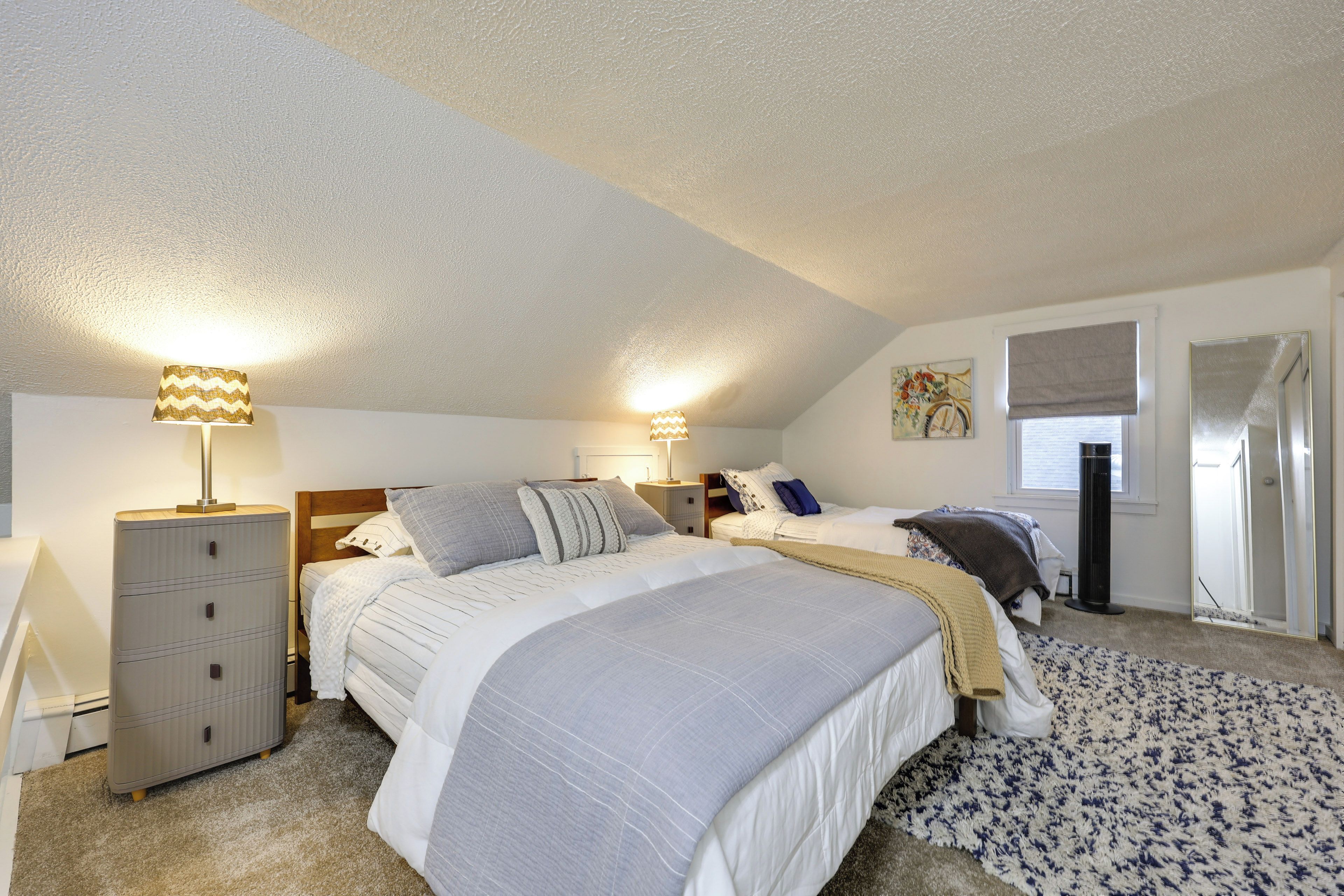 A bedroom with two beds, a dresser, a radiator, and a window with curtains.