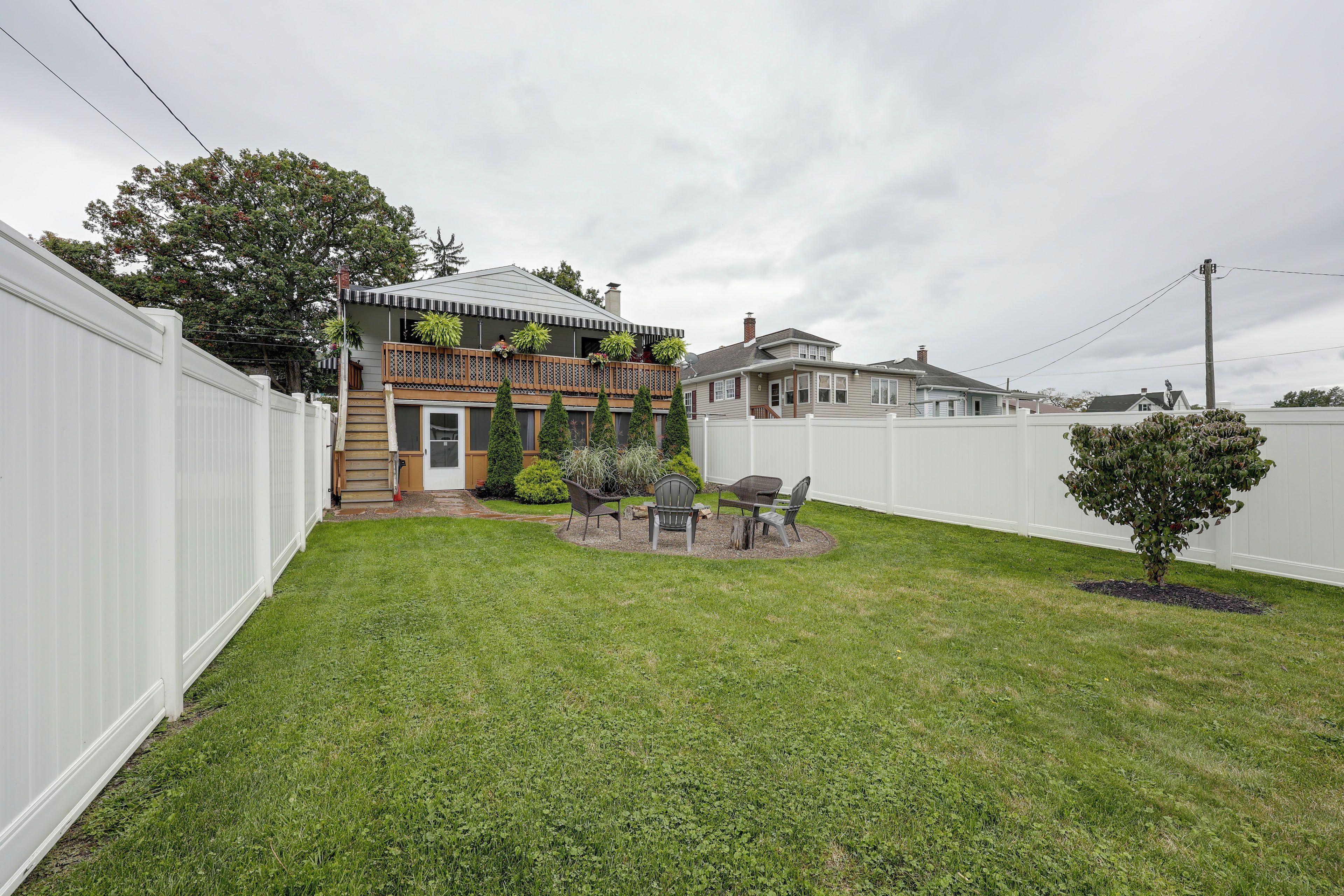 A residential property with a fenced yard, a small patio with outdoor furniture, and a variety of plants.