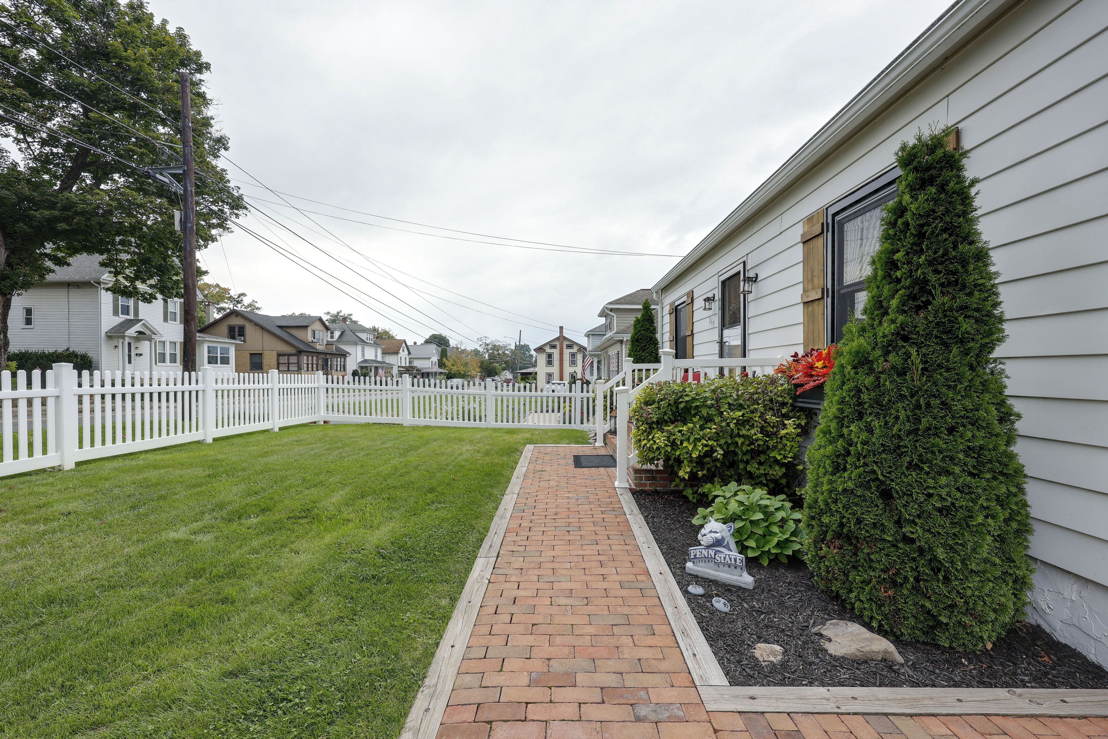 A residential property with a paved driveway, a white picket fence, and a well-maintained lawn.