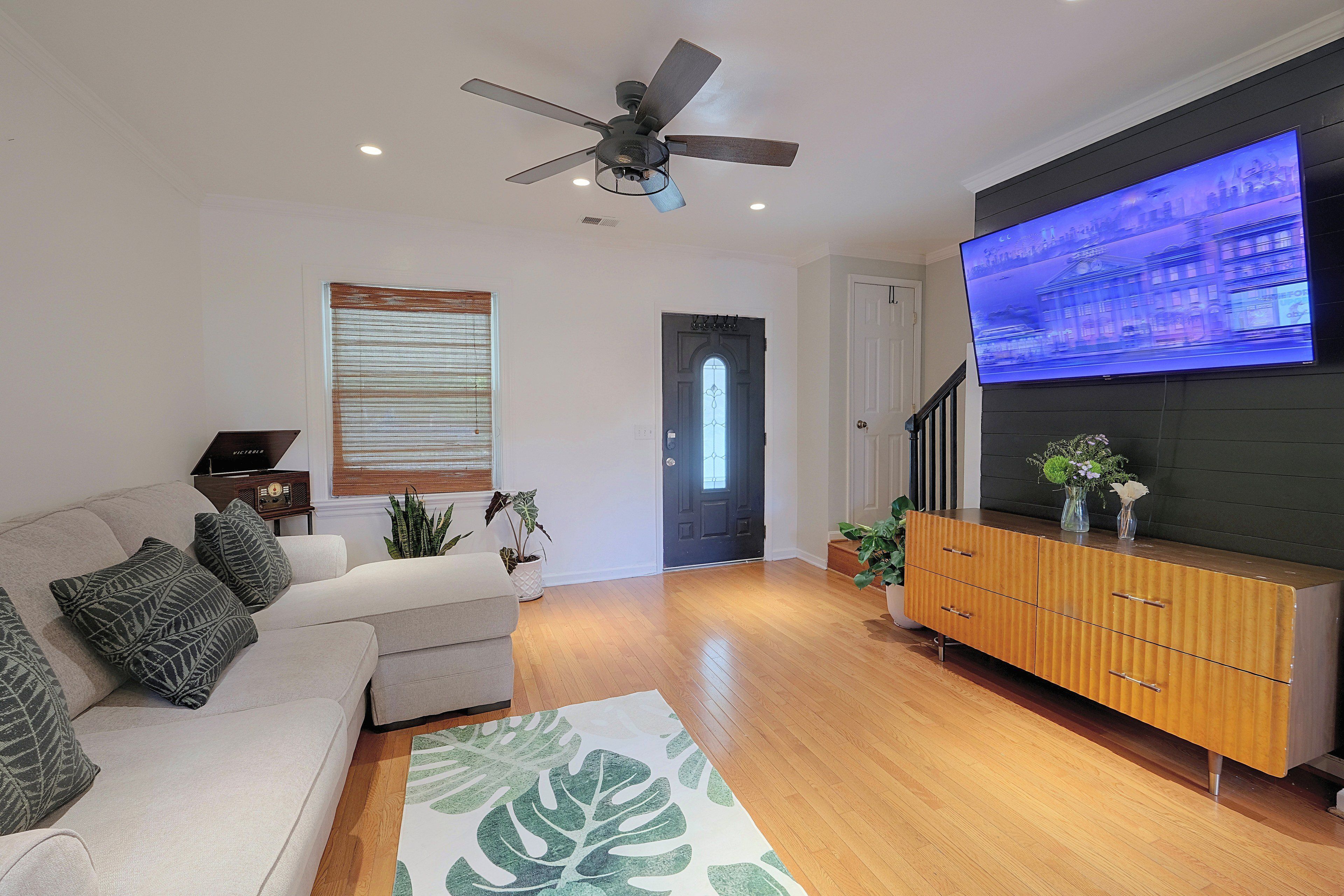 A modern living room with a flat-screen TV, a ceiling fan, a sofa, a wooden cabinet, and a door.