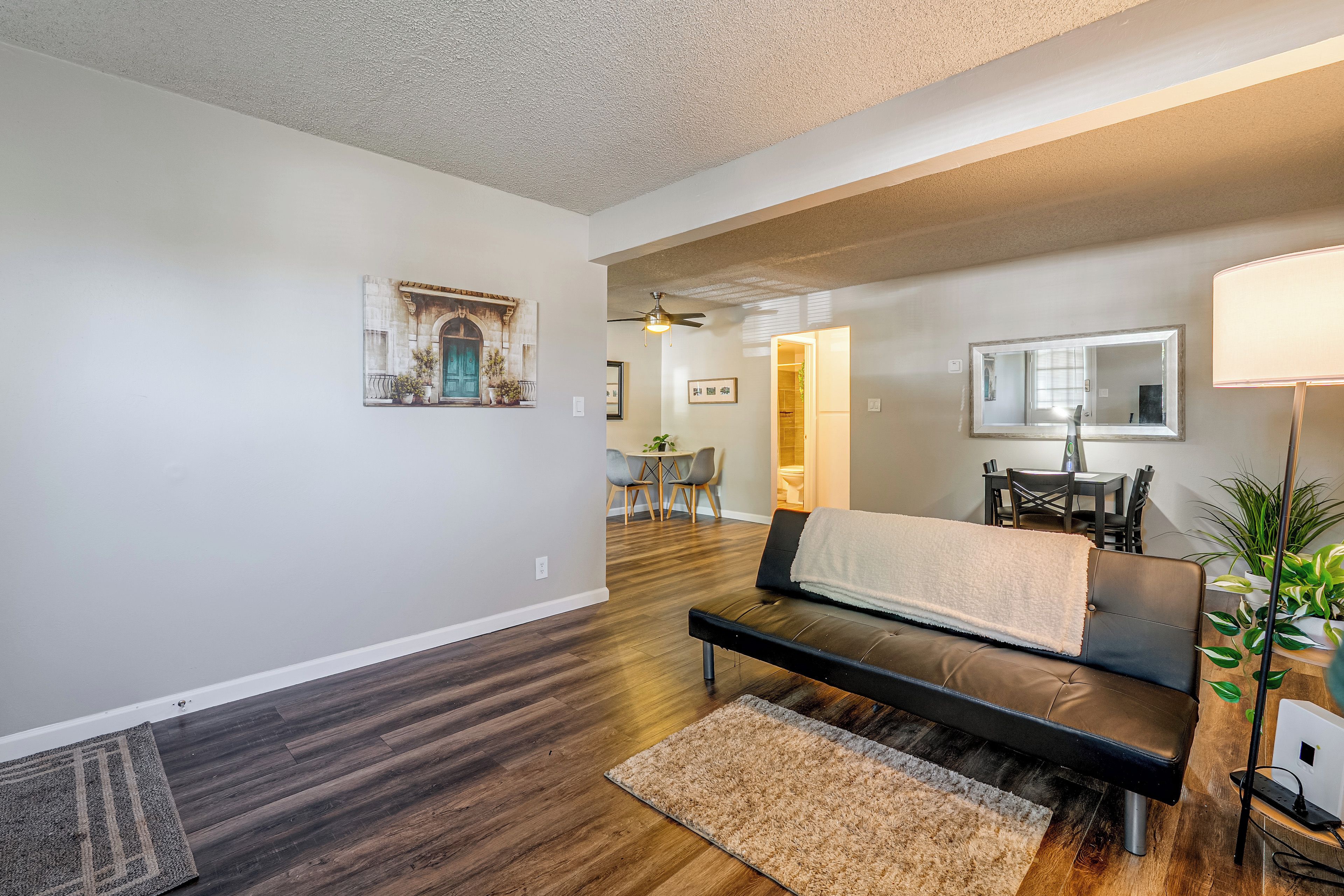 Un salon moderne avec un canapé, un coin repas comprenant une table et des chaises, un couloir menant à une salle de bain et un ventilateur de plafond.