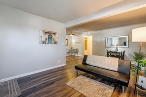 Un salon moderne avec un canapé, un coin repas comprenant une table et des chaises, un couloir menant à une salle de bain et un ventilateur de plafond.