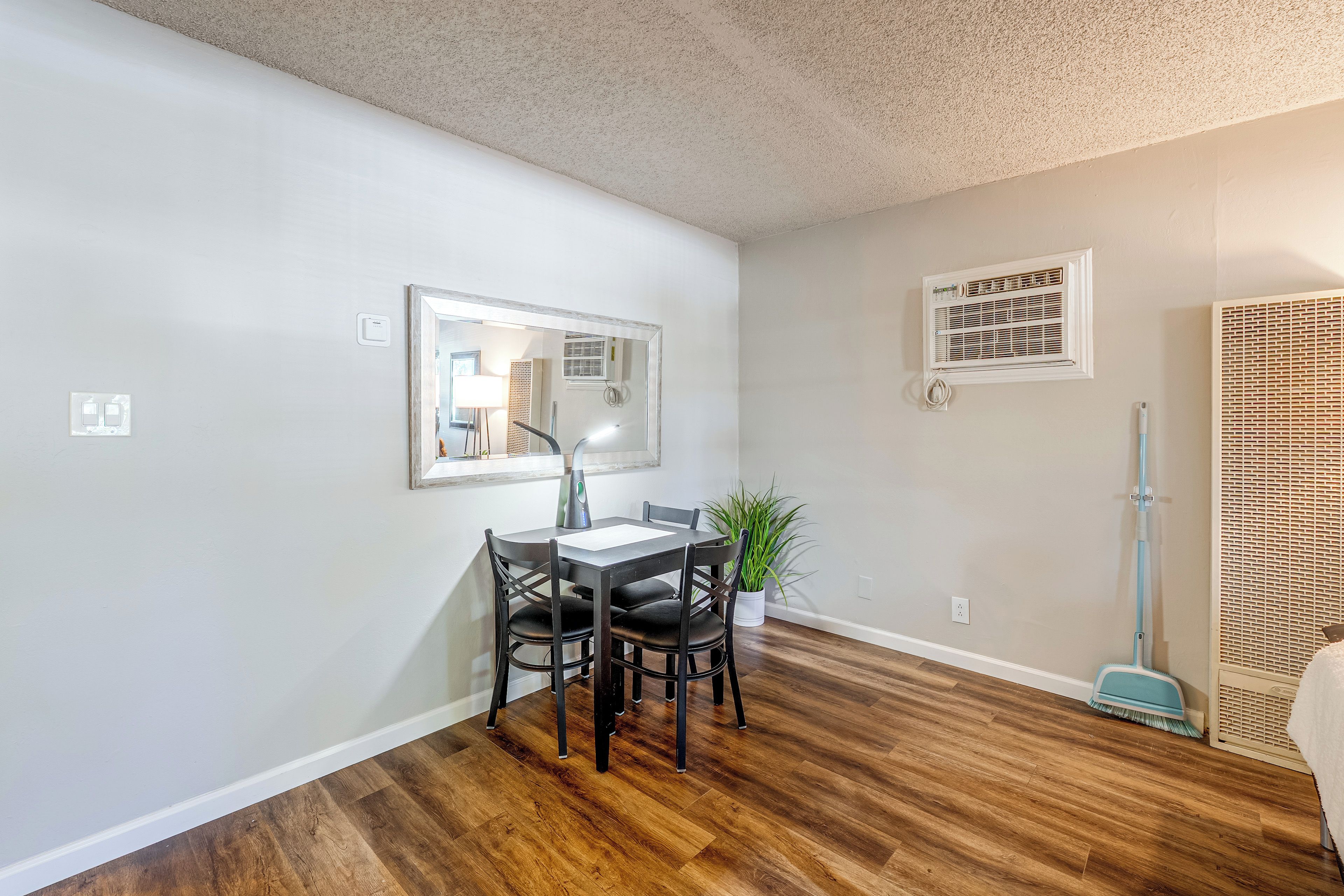 A dining area with a table and chairs, a mirror on the wall, and an air conditioning unit.