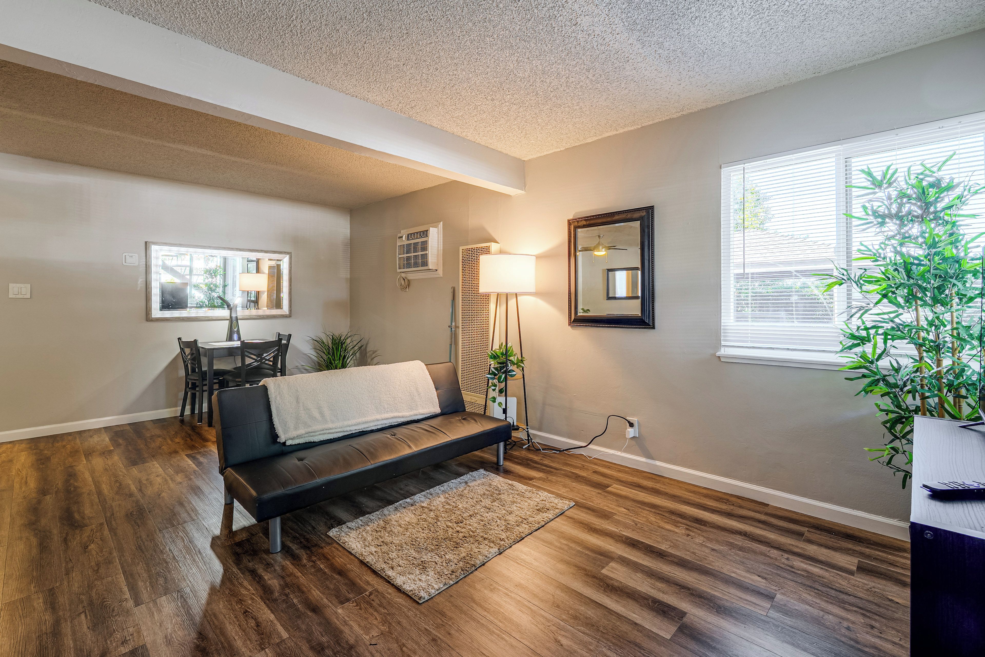 A living room with a sofa, a dining area with a table and chairs, a large window with blinds, and a ceiling fan.