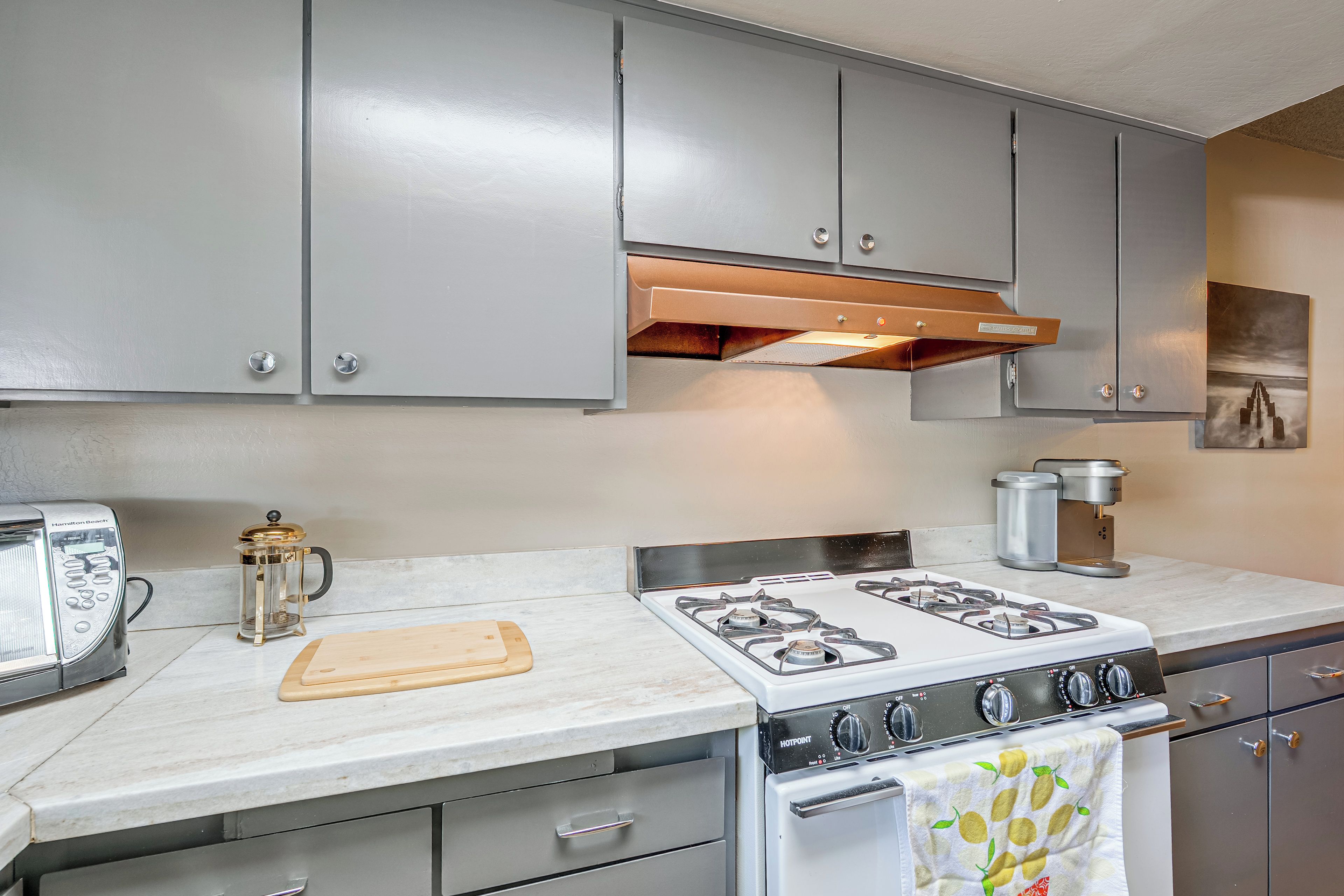 Una cocina con estufa a gas, cafetera y jarra de Hamilton Beach.