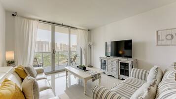 Una sala de estar moderna con un sofá, una mesa de centro, un televisor y un balcón con vistas a la ciudad.
