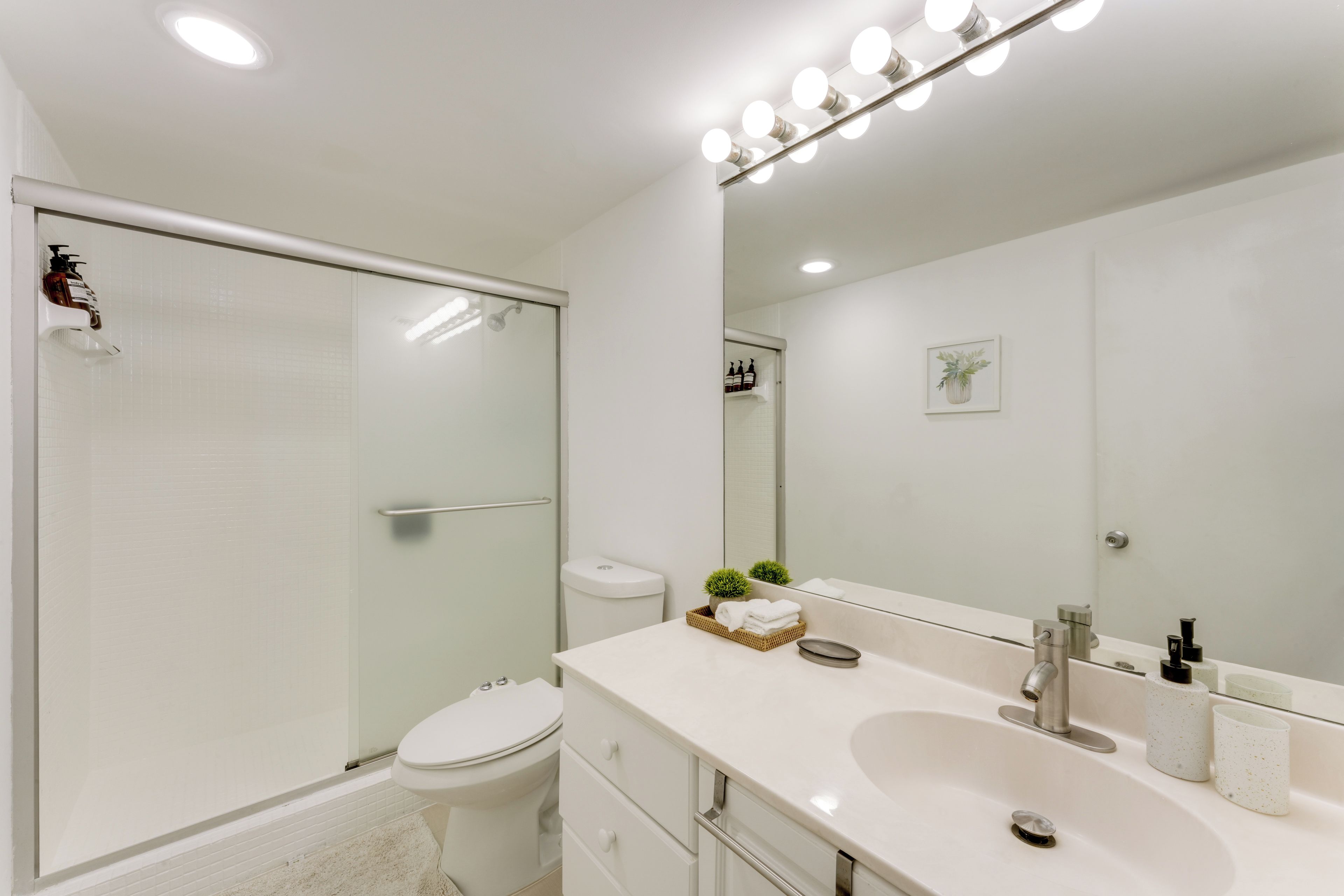 Un baño moderno con cabina de ducha de vidrio, inodoro blanco, tocador con lavamanos y un espejo grande.