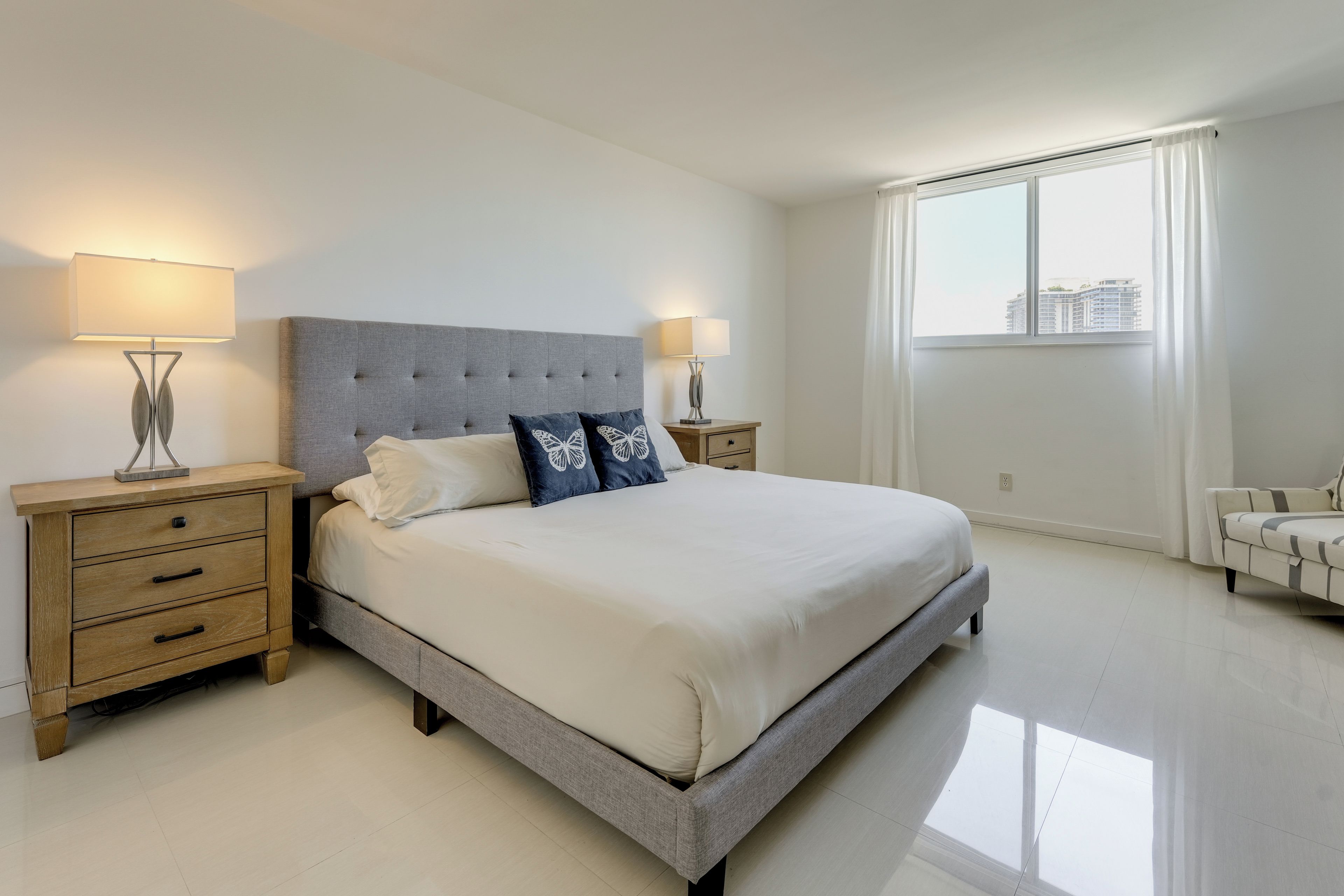 Un dormitorio con cama, mesitas de noche, ventana y vistas a edificios.