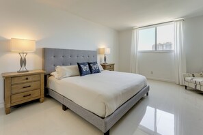 Un dormitorio con cama, mesitas de noche, ventana y vistas a edificios.