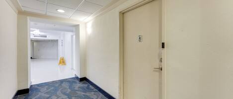 A hotel hallway with a carpeted floor, a door on the right, and a caution sign on the left.